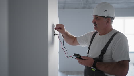 A-man-electrician-checks-the-voltage-in-the-network-with-a-wire-tester-preparing-to-install-a-smart-home.-Inspection-of-all-systems-by-a-professional-electrician